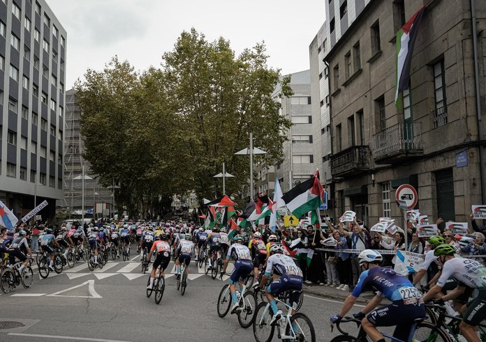 Peloton a v pozadí lidé s palestinskými vlajkami.