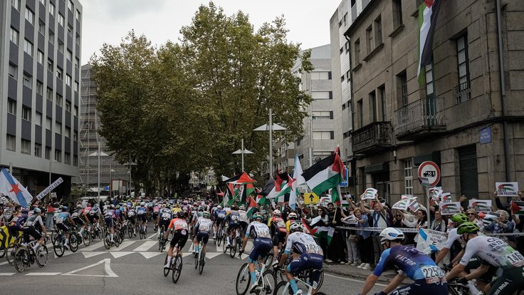 Peloton a v pozadí lidé s palestinskými vlajkami.